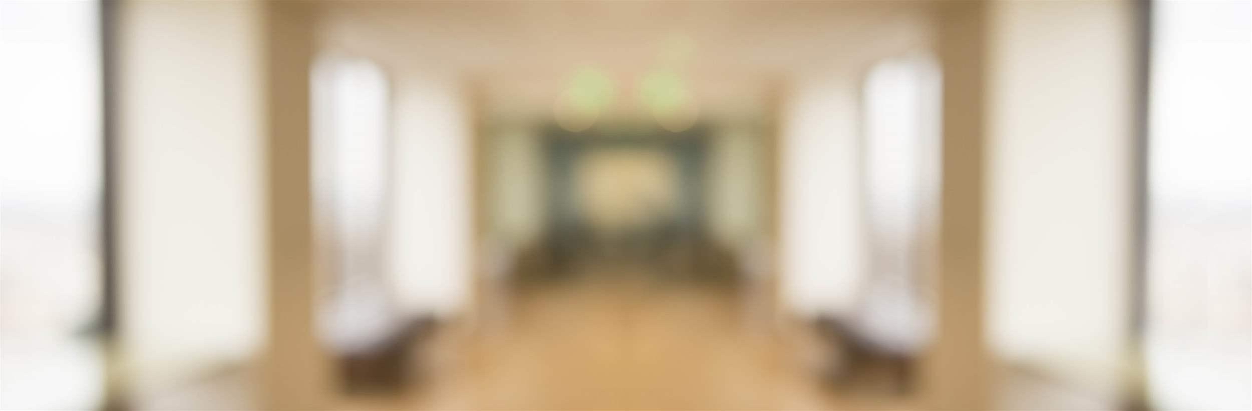 A blurry panoramic photograph of an office corridor with overhead lighting