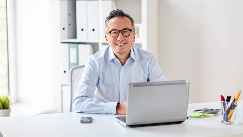 business, people and technology concept - happy smiling businessman in eyeglasses with laptop computer office