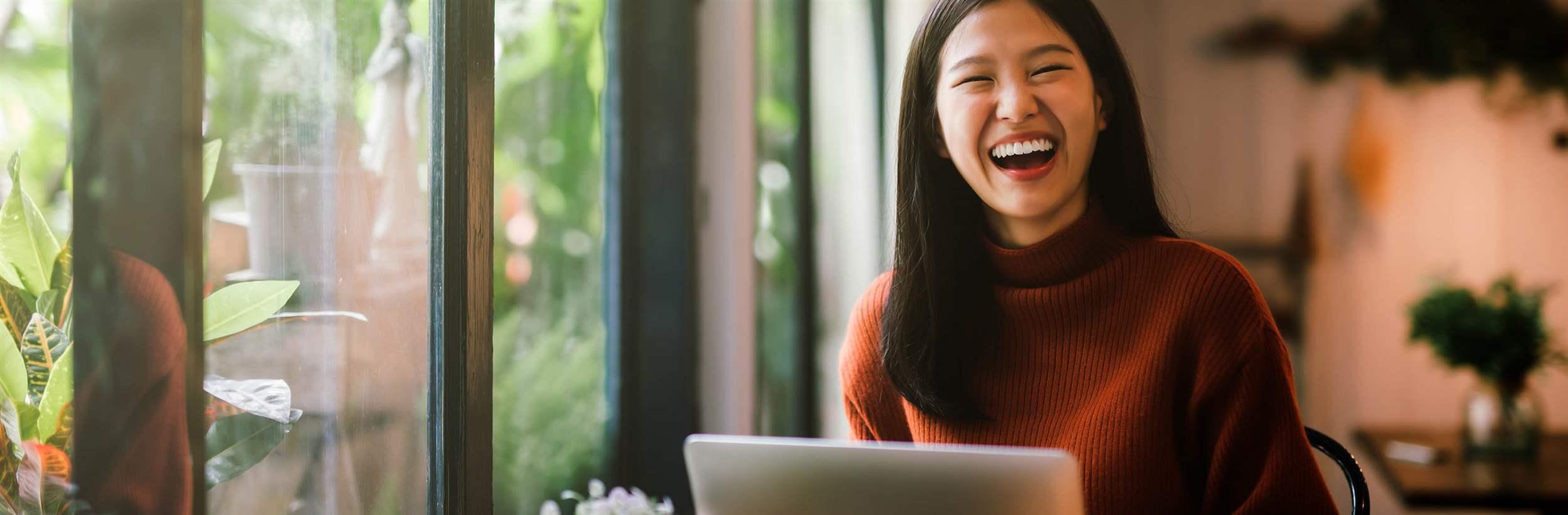 Happy young asian girl working at a coffee shop with a laptop