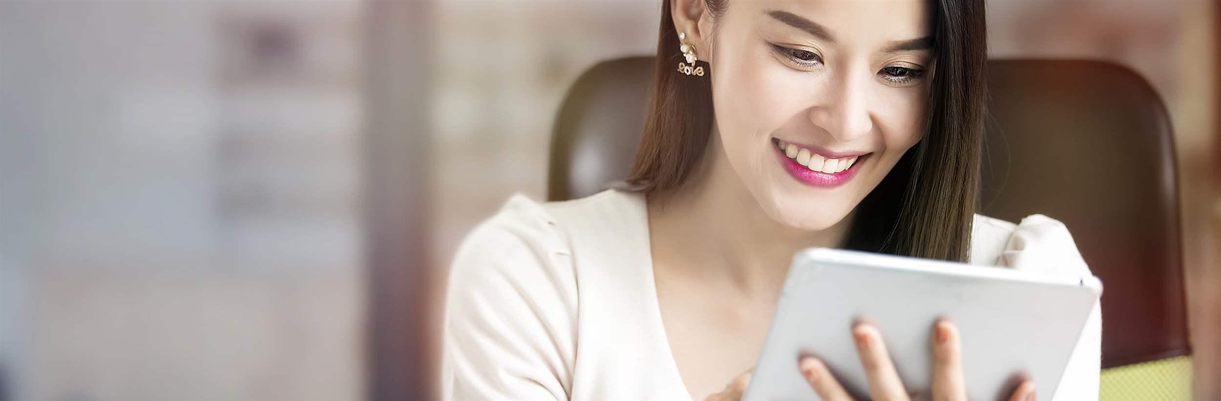 Beautiful woman smiling and using tablet while sitting at office desk.