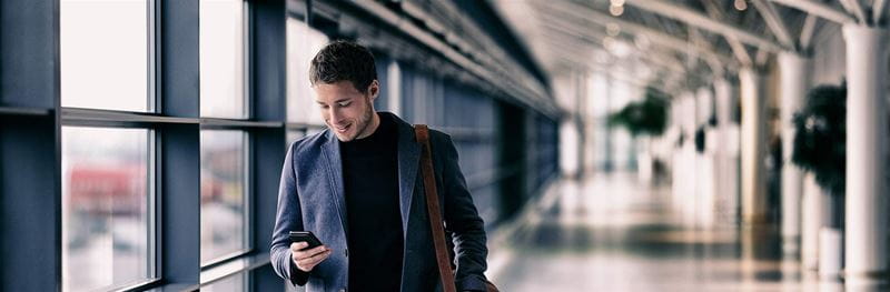 Business man texting on mobile phone at airport on business trip using cellphone texting sms message on smartphone app - young businessman commuter lifestyle panoramic banner.