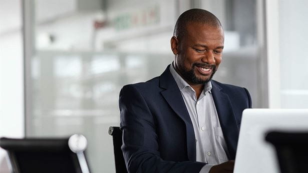 Positive mature businessman working on laptop in modern office. Successful african business man working on computer while sitting at desk. Smiling middle aged man working in a corporate.